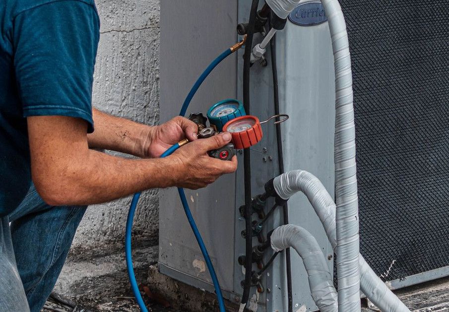 Technician repairing an air conditioner unit outdoors, wearing a facemask and using a manifold gauge.